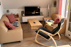 Una sala de estar moderna con un sofá, un sillón mecedora, una mesa de centro y un televisor de pantalla plana.
