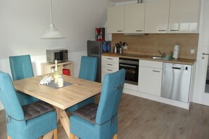 Cocina compacta con comedor, que incluye una mesa de madera, sillas azules, microondas, refrigerador, cafetera y lavavajillas.