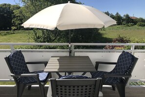A deck with a table and two chairs, an umbrella, and a view of a green landscape. - Vacation apartment in a quiet location and with balcony - Ferienhaus Solamar FeWo OG - (Breege)