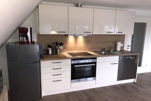 A modern kitchen with white cabinets, a stainless steel refrigerator, a built-in oven, and a dishwasher.