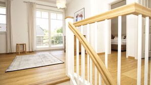 Une pièce spacieuse avec un plancher en bois, un escalier blanc et une vue dégagée sur l’extérieur grâce à une grande fenêtre.