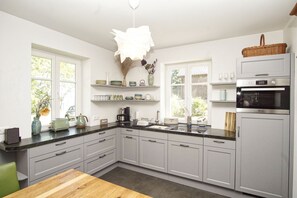 Une cuisine moderne avec des meubles gris, une table en bois, un luminaire suspendu et un four encastré.