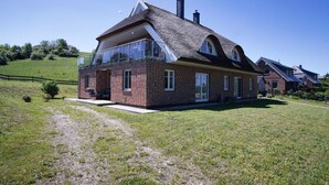 Une maison à deux étages, avec une façade en briques, de grandes fenêtres et un toit de chaume.