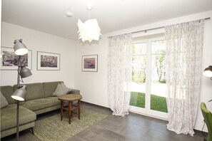 A living room with a sofa, a small round table, a floor lamp, and a large window with curtains. - Rohrweihe Vacation Home - a beachfront vacation home with ocean views in a quiet location - (Gager)