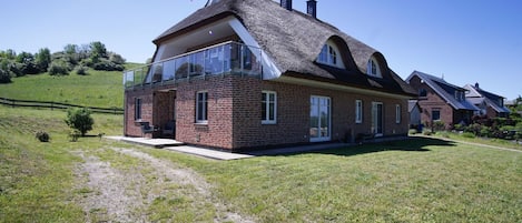 A two-story house with a brick exterior, large windows, and a thatched roof.