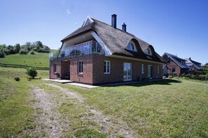 A two-story house with a brick exterior, large windows, and a thatched roof.