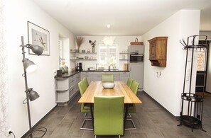 A modern kitchen with a wooden dining table, green chairs, and a hanging light fixture. - Vacation home Rohrweihe - waterfront vacation home with sea view in a quiet location - (Gager)