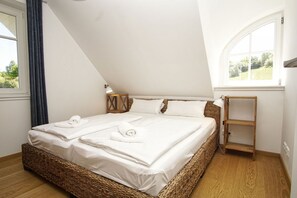 Quarto com cama grande, mesa de cabeceira, abajur, cadeira de vime e janela.