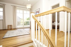 A spacious room with a wooden floor, a white staircase, and a view through a large window.