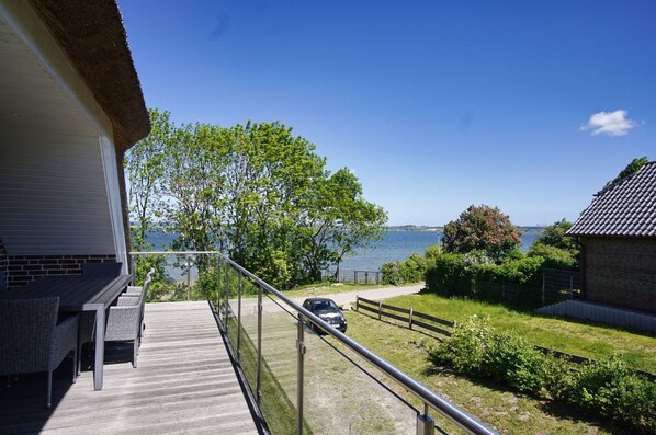 A balcony with a view of the sea, a car parked on the driveway, and a building with a brick facade.