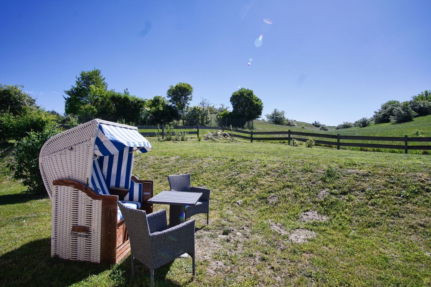 A wicker chair and table set up in a grassy outdoor area with a wooden fence in the background.