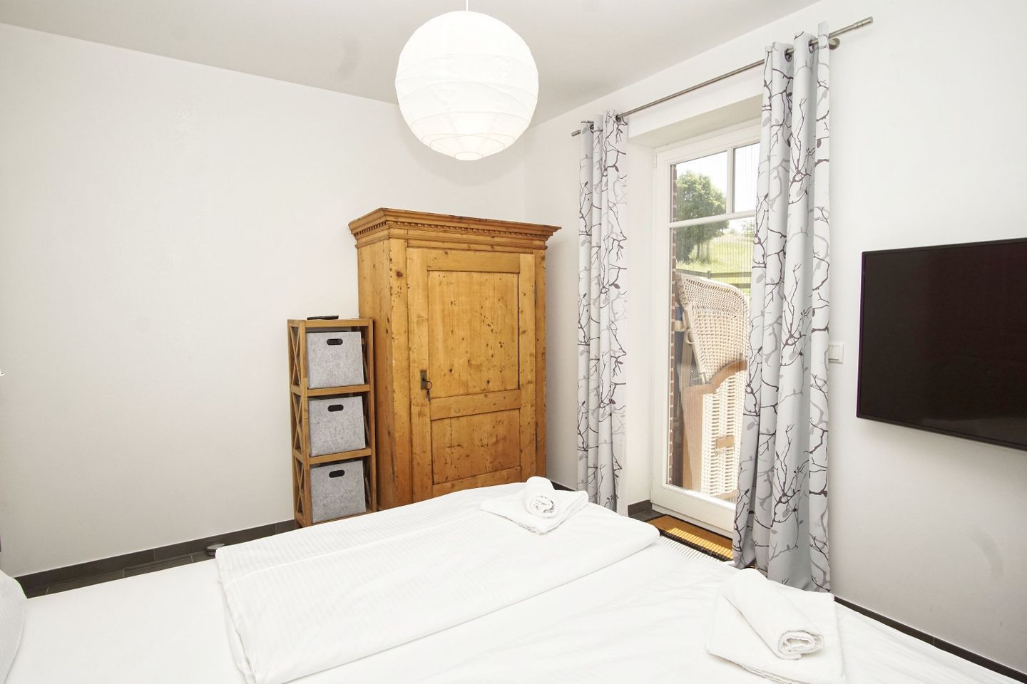 Una camera da letto con un letto, un armadio in legno, una TV e una finestra con tende.