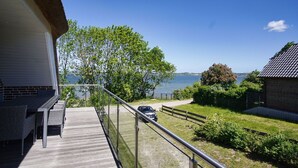 Un balcon donnant sur la mer, une voiture garée dans l’allée, et un bâtiment à la façade en briques.
