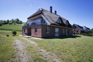 A two-story house with a brick exterior, large windows, and a thatched roof.