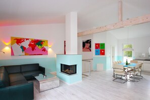 A modern living room with a fireplace, a black sofa, a colorful map, and a dining area with chairs. - Close to the beach, balcony, ocean view, sauna, free adventure pool - Palstek Beach House - (Göhren)