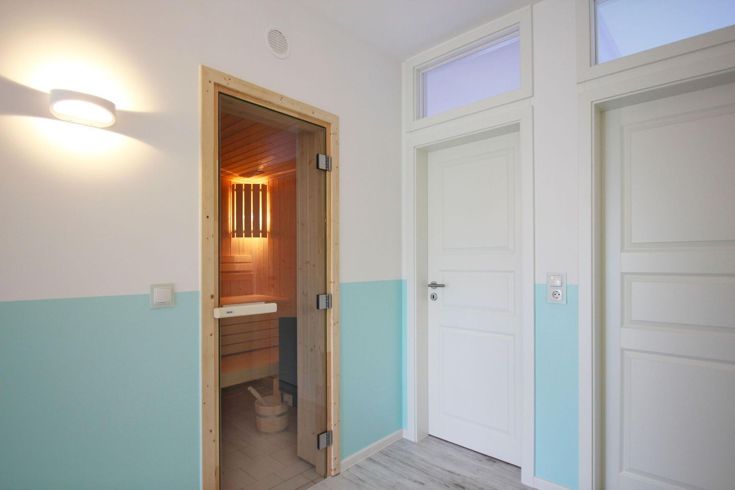 Un couloir avec un sauna en bois, des portes blanches et un interrupteur sur le mur.