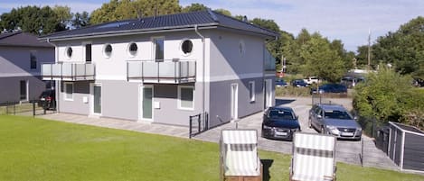 Ein modernes, zweistöckiges Gebäude mit flachem Dach, zahlreichen Fenstern und einem Parkplatz mit Autos.