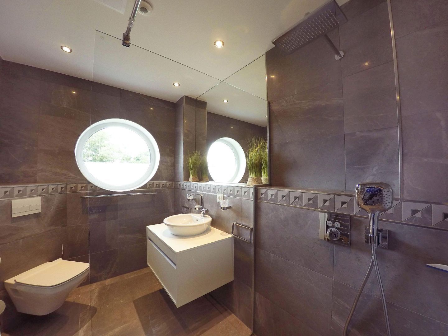 A modern bathroom with a round window, a toilet, a sink, and a shower area.