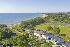 Vue aérienne d’une zone résidentielle côtière, avec des maisons, une plage et un terrain de sport.