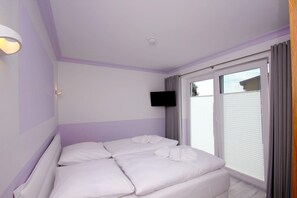 A bedroom with a bed, a flat-screen TV mounted on the wall, and a window with blinds. - Close to the beach, balcony, ocean view, sauna, free adventure pool - Schotstek Beach House (Göhren)