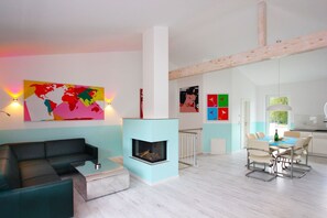 A modern living room with a fireplace, a dining area with a table and chairs, and a kitchen visible through an open door. - Close to the beach, balcony, ocean view, sauna, free adventure pool - Schotstek Beach House (Göhren)