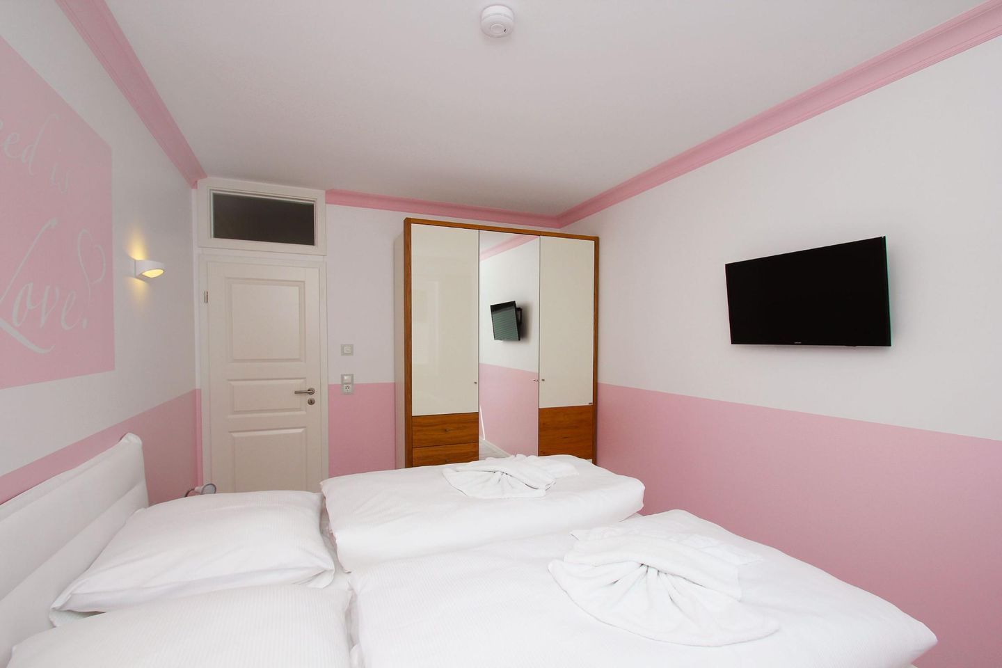 Une chambre d’hôtel avec un lit, un téléviseur fixé au mur et une porte donnant sur une autre pièce.