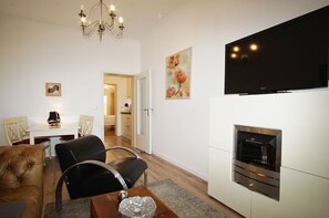 A modern living room with a fireplace, a dining area with a table and chairs, and a TV mounted on the wall.