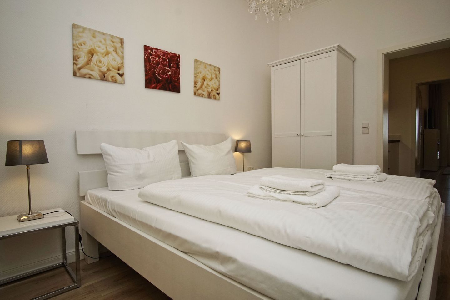 A neatly made bed with white linens and pillows, a bedside table with a lamp, and a wardrobe in a hotel room.