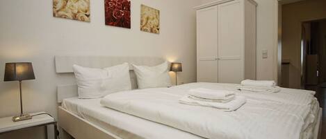 A neatly made bed with white linens and pillows, a bedside table with a lamp, and a wardrobe in a hotel room.