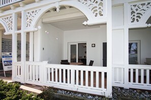 Un edificio blanco con un porche cubierto, un área de comedor con sillas y un cartel.