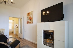 A modern living room with a fireplace, a flat-screen TV mounted above it, and a dining area with chairs.