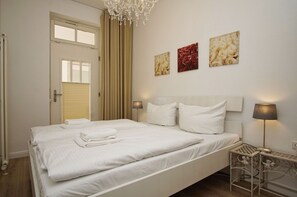 A neatly made bed with white linens, a chandelier, and three framed pictures on the wall. - Villa Seeadler - Die Ferienwohnung in der Villa Seeadler (Binz)