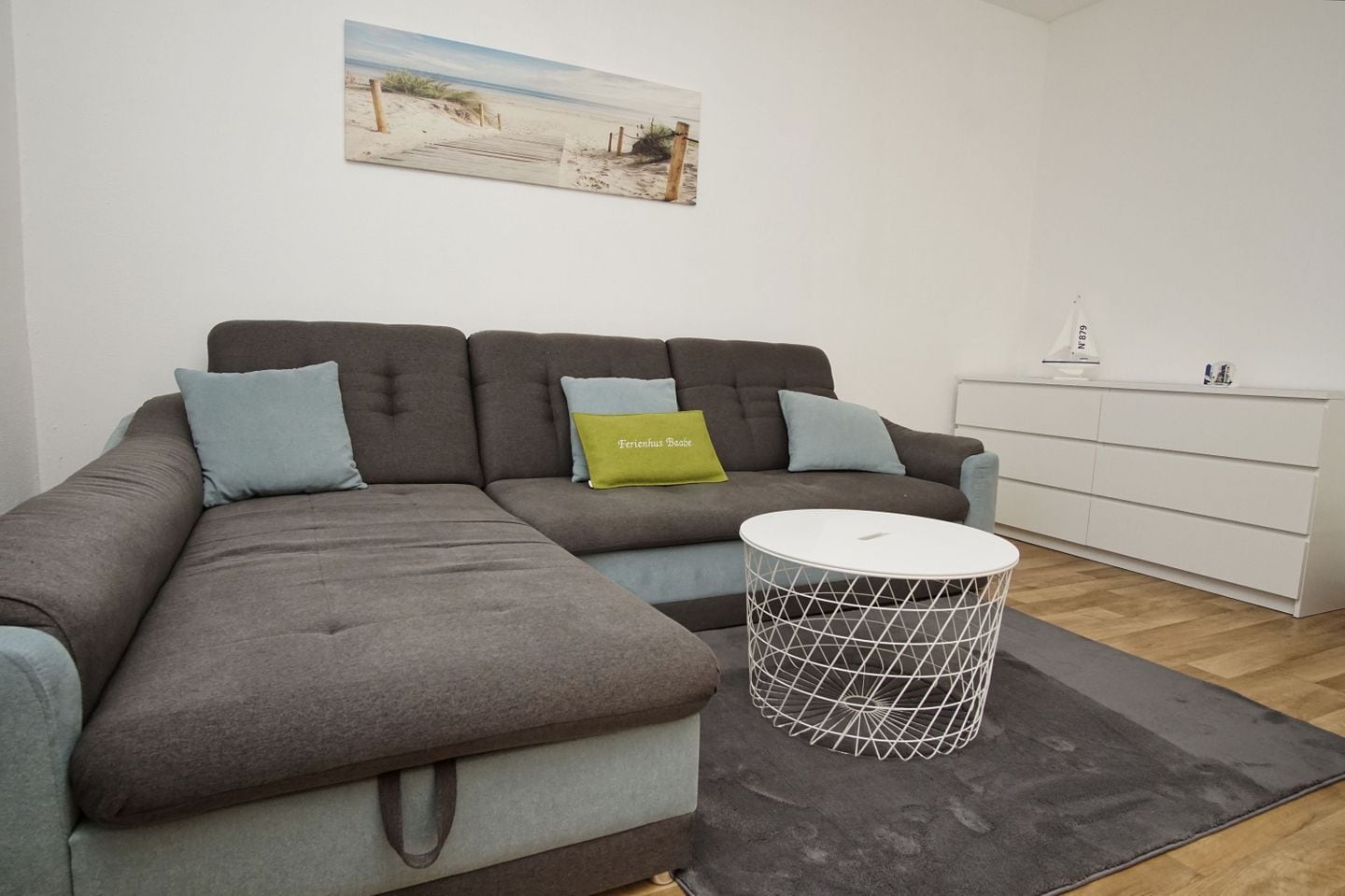 A modern living room with a sectional sofa, a round coffee table, and a minimalist white cabinet.