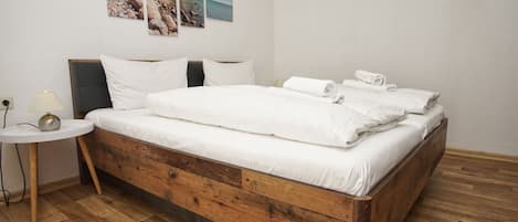 A bedroom with a wooden bed, white bedding, a bedside table with a lamp, and a wall with three framed pictures.