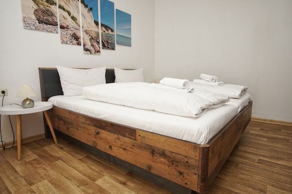 A bedroom with a wooden bed, white bedding, a bedside table with a lamp, and a wall with three framed pictures.
