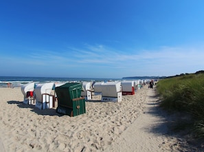 A beach with rows of beach huts, a sandy path, and the ocean in the background.