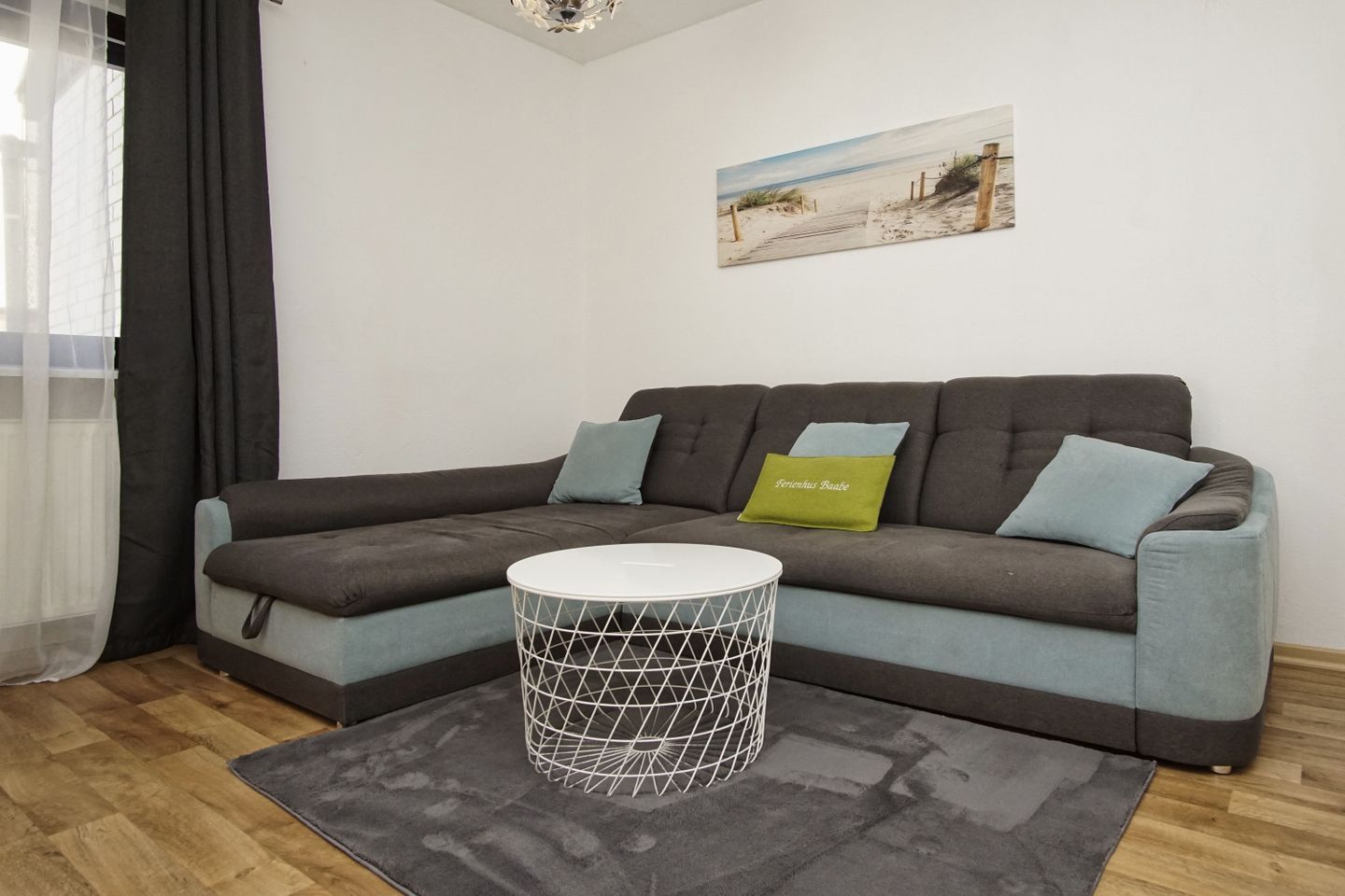A modern living room with a sectional sofa, a round coffee table, and a beach-themed artwork on the wall.
