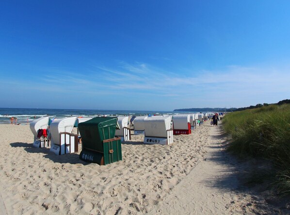 A beach with rows of beach huts, a sandy path, and the ocean in the background.