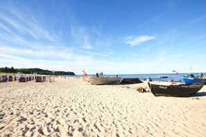 A sandy beach with boats, umbrellas, and beachgoers.