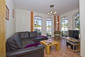 Ein Wohnzimmer mit Ledersofa, einem Holztisch, einem Korbstuhl und einem Fernseher auf einem Holzschrank.