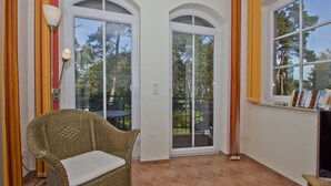 A room with a wicker chair, a table, and a bookshelf. - Kurparkresidenz - close to the beach, free use of the AHOI adventure pool and sauna - (Baabe)