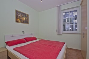 Une chambre à coucher avec un lit, une table de chevet, une fenêtre avec des rideaux et une affiche accrochée au mur.
