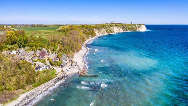 Un pueblo costero con casas a lo largo de la playa, un litoral rocoso y una vista despejada del mar.