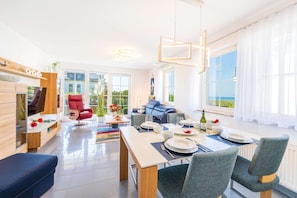 A modern living room with a dining area, large windows, and a view of the outdoors.