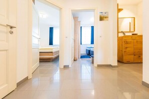 A hallway leading to a bedroom with a bed, a wooden wardrobe, and a bathroom with a mirror and sink.