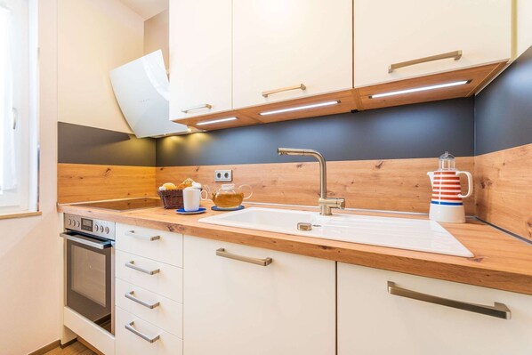 Una cocina moderna con encimeras de madera, horno empotrado, lavabo con grifo moderno y hervidor sobre la encimera.