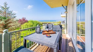 Un balcón con una mesa dispuesta para dos personas, con vistas a un paisaje marino y vegetación.