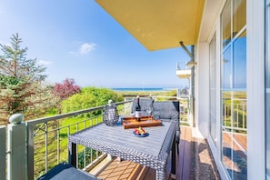 A balcony with a table set for two, overlooking a scenic view of the sea and greenery.