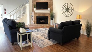 Ein Wohnzimmer mit Kamin, zwei Sofas, einem Couchtisch und einem Fernseher, der über dem Kamin angebracht ist.