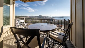 Varanda com mesa redonda e cadeiras, com vista panorâmica para um castelo distante e um corpo d'água.